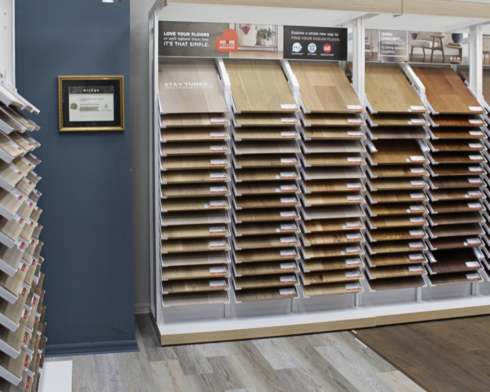 A display of various hardwood flooring samples in flooring showroom with Adore your floors guarantee signage above them.
